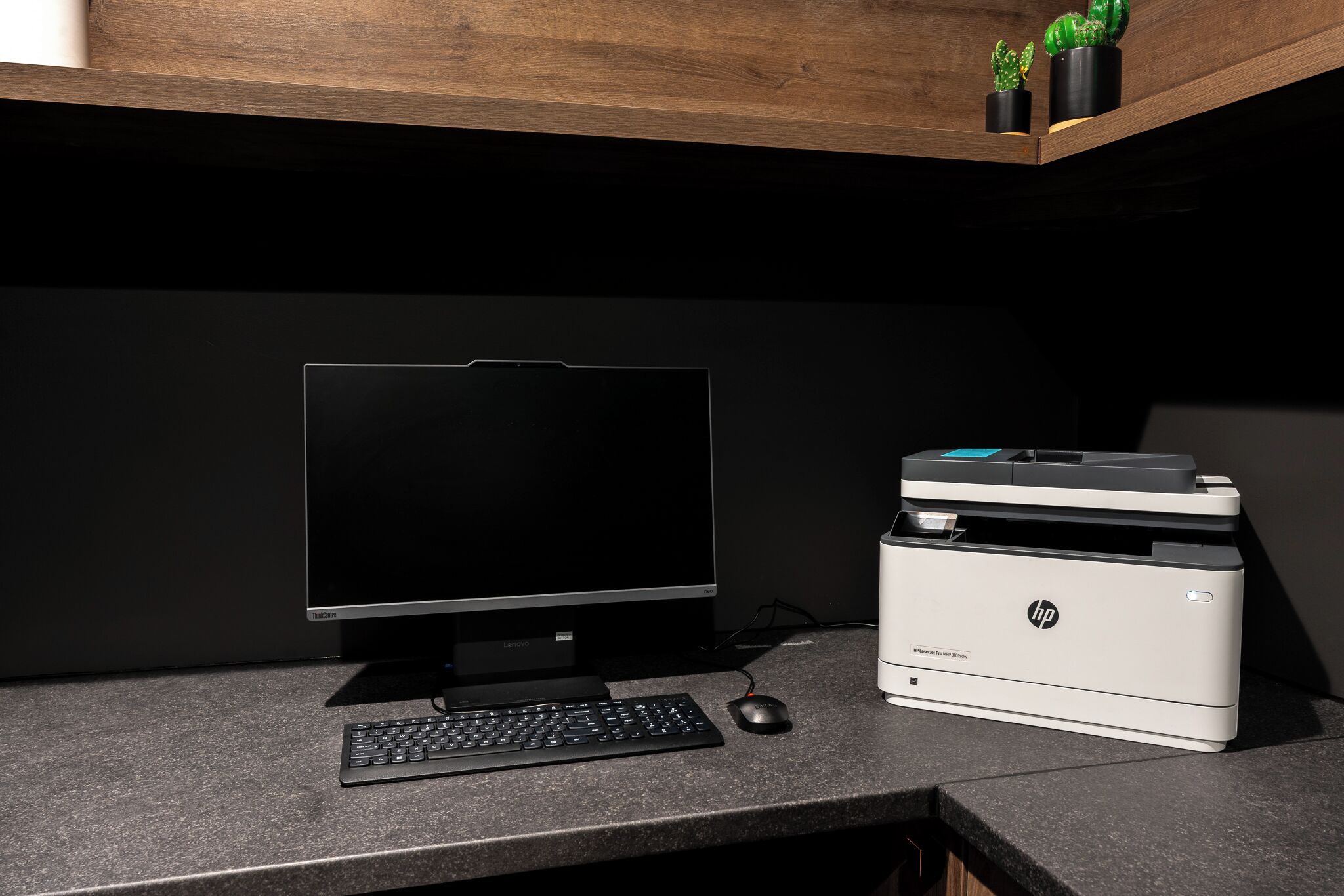 Ein Schreibtischcomputer mit Monitor, Tastatur, Maus und einem HP-Drucker auf einer dunklen Arbeitsplatte.