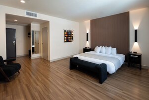 Una camera d'albergo moderna con un letto grande, una panca, una scrivania e un'opera d'arte appesa al muro.