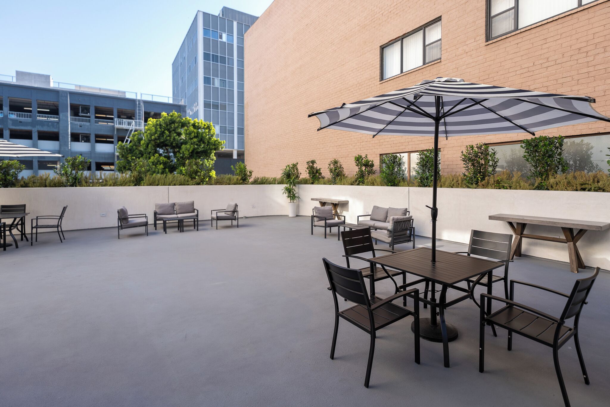 Un patio al aire libre con una mesa y sillas, un paraguas a rayas y un edificio al fondo.