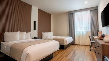 A hotel room with two beds, a desk, a chair, a TV, and a large window with curtains.