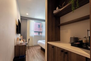 Ein modernes Hotelzimmer mit einem Bett, einem Schreibtisch mit Stuhl, einem an der Wand befestigten Fernseher und einem Vorhangfenster.