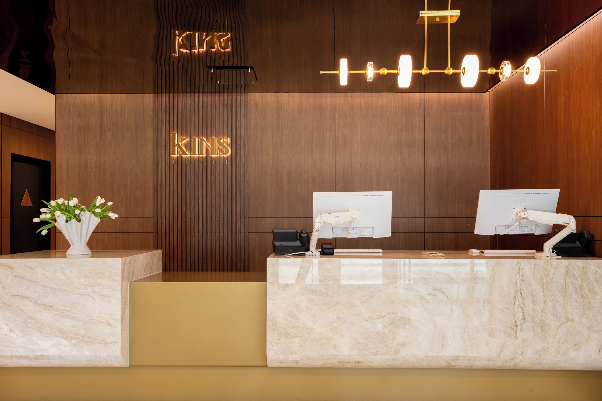 A reception desk with a marble top, two computer monitors, a cash register, and a vase with flowers.