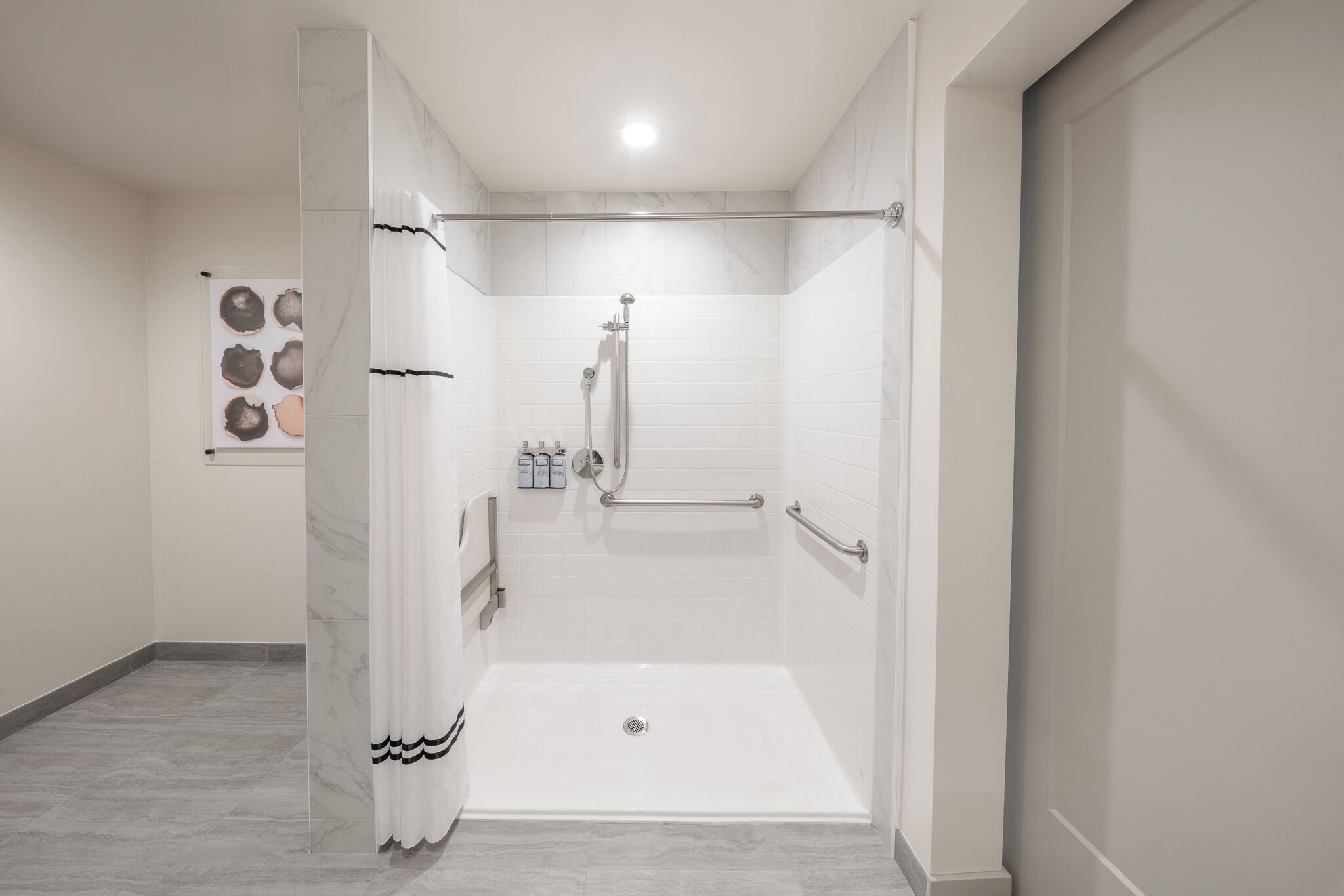 Un baño moderno con ducha a ras de suelo, barras de apoyo y suelo de baldosas.