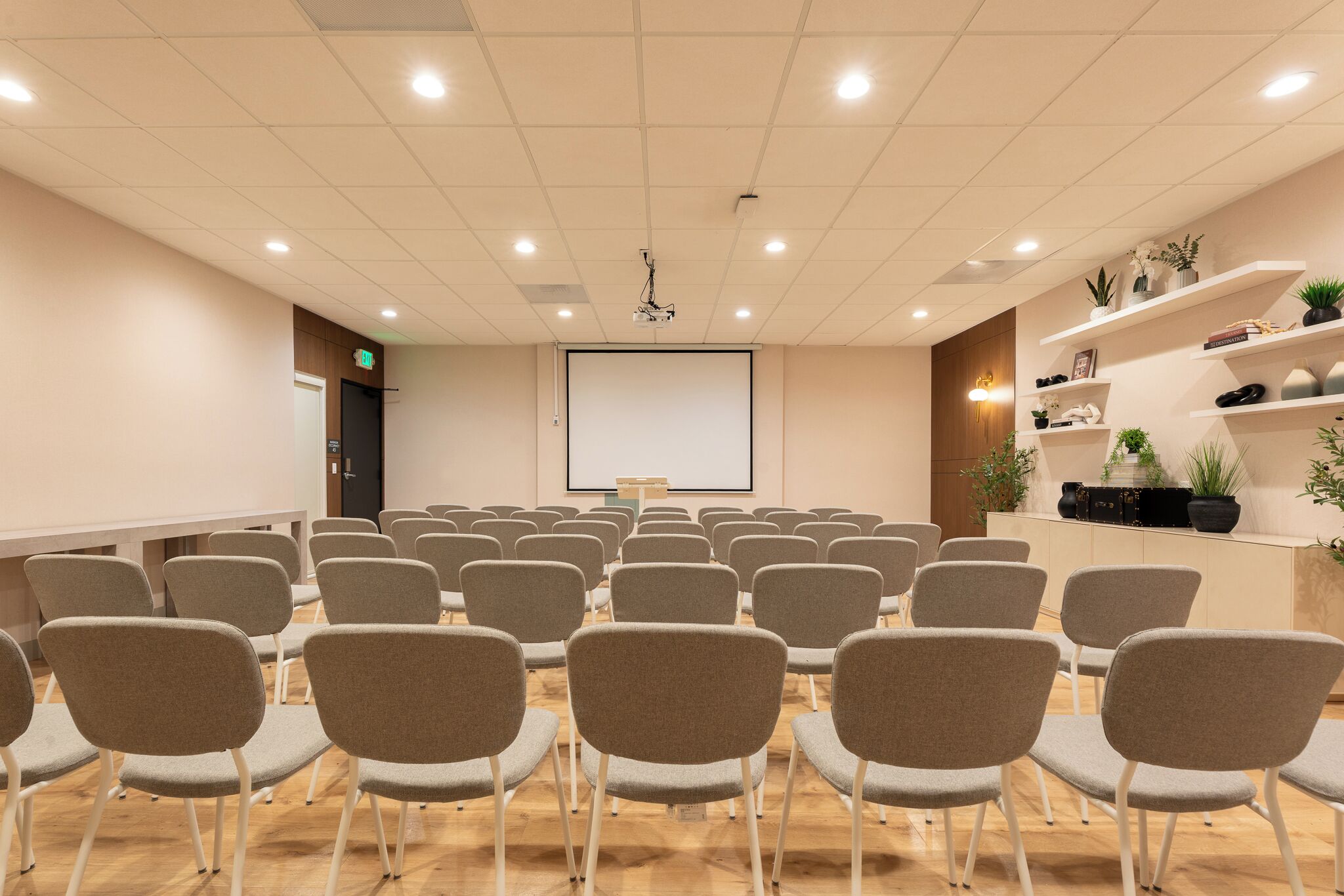 A conference room with rows of chairs, a projector screen, and a wooden floor.