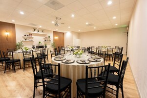 Uma sala de conferências com mesas redondas, cadeiras pretas e toalhas de mesa brancas.