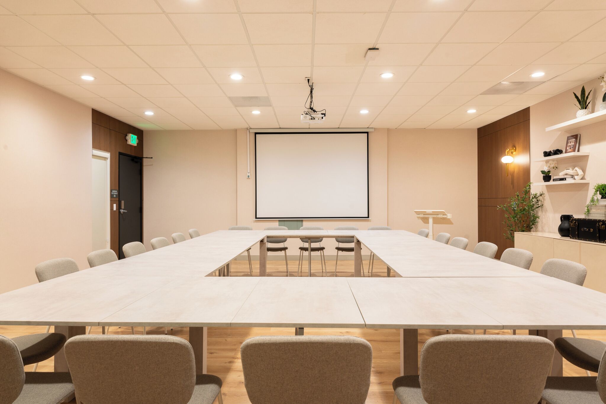 A conference room with a long table, chairs, a projector screen, and a door.