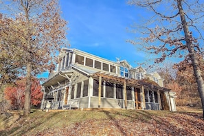 A two-story house with a covered porch, surrounded by trees with autumn foliage. - Gray Goose Manor | Lakefront, Fire Pit, Lake Views, Amazing Sunsets! (Stigler)