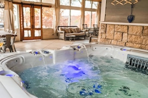 A hot tub with water jets, a stone wall, and a view of a patio area with outdoor furniture. - Gray Goose Manor | Lakefront, Fire Pit, Lake Views, Amazing Sunsets! (Stigler)