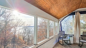 A covered porch with large windows, a rocking chair, and a table. - Lakefront Oasis | Hot Tub | Game Room | 3+ Acres (Stigler)