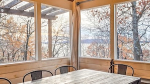 A room with a wooden table and chairs, large windows with a view of trees and a body of water. - Lakefront Oasis | Hot Tub | Game Room | 3+ Acres (Stigler)