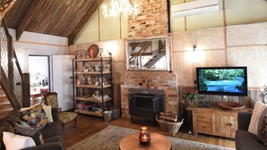 Un salón rústico estilo loft con vigas de madera a la vista, chimenea de ladrillo, televisor y asientos cómodos.