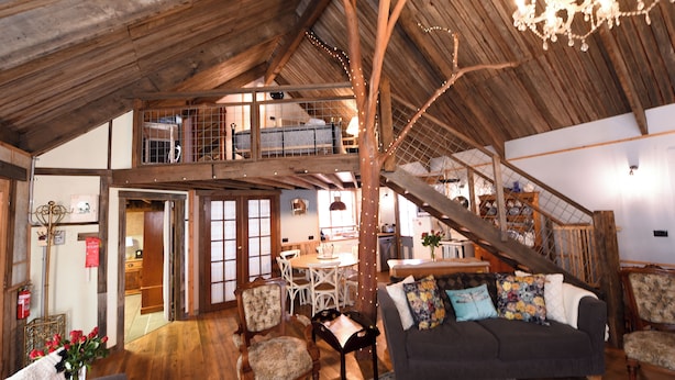 Un loft espacioso con techo alto, vigas de madera, un comedor y una escalera que sube a un nivel superior.