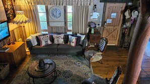 Una sala de estar acogedora con un sofá gris oscuro, cojines estampados, una mesa de centro de madera y un reloj antiguo en la pared.
