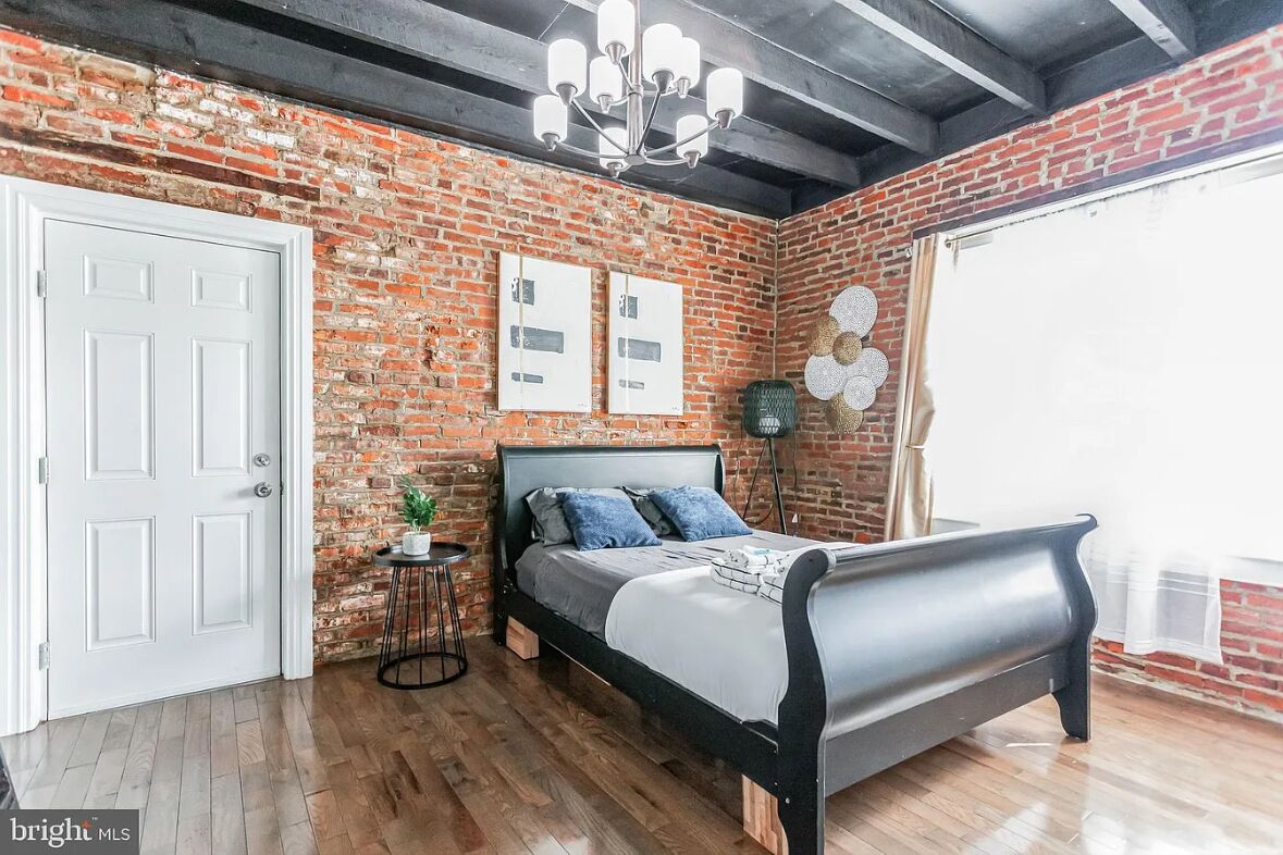 Une chambre avec un mur en briques, un lit, un lustre et une porte.