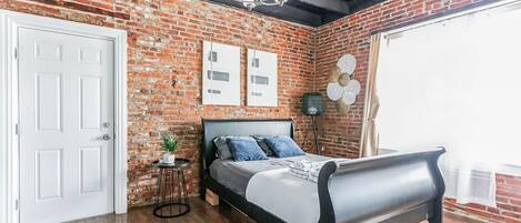 Une chambre avec un mur en briques, un lit, un lustre et une porte.