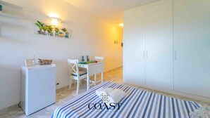 A bedroom with a bed, a desk, a chair, a wardrobe, and a small refrigerator. - Blue Skyline | Sea View Terrace in Portisco (Olbia)
