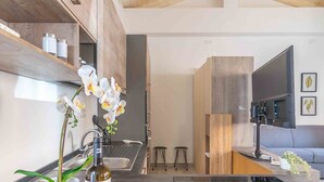 A modern kitchen with a built-in oven, a sink, and a countertop. There are two stools and a television on a stand. - St. Simplicius - 5 mins from city center, WiFi, AC (Olbia)