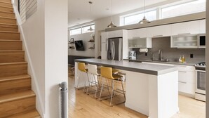 A modern kitchen with a central island, bar stools, stainless steel appliances, and pendant lighting.