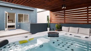 A modern outdoor pool area with a wooden ceiling, a hot tub, and a seating area.