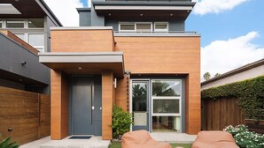 A modern two-story house with a front door, a small porch, and a glass door leading to a patio area.