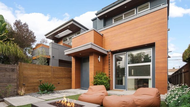A modern house with a flat roof, large windows, and a fire pit in the backyard.