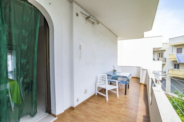 Ein Balkon mit Tisch und Stühlen, einem grünen Vorhang und einer weißen Wand.