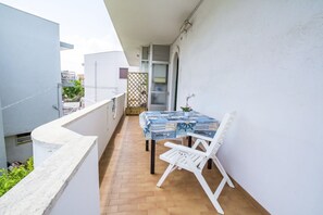 Un balcón con una mesa y sillas, una planta pequeña en maceta y una ventana con vistas a edificios.