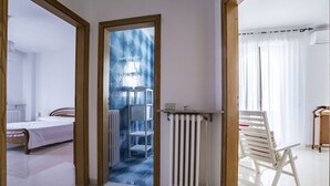 Ein Hotelzimmer mit Bett, Heizkörper, Stuhl und Blick durch eine Tür.