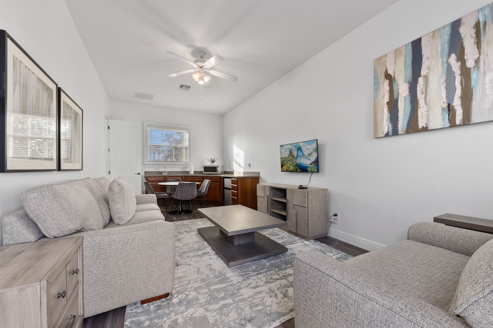 A modern living room with a sofa, a coffee table, and a TV. There is a kitchen in the background with a microwave and cabinets.
