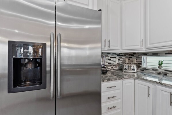 Un refrigerador de acero inoxidable con dispensador de agua incorporado, gabinetes blancos y un protector contra salpicaduras de azulejos.