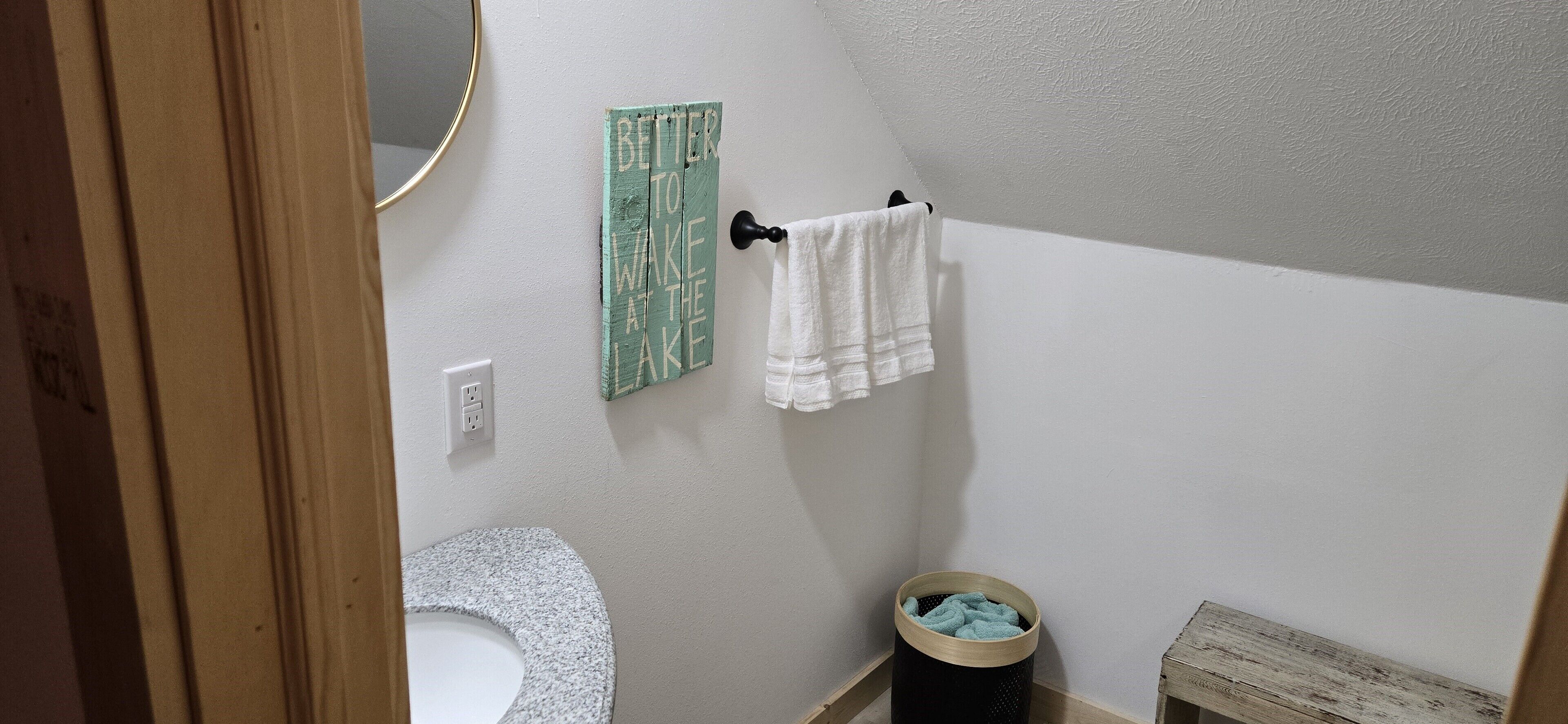 A bathroom with a white sink, a towel rack with a white towel, a green sign on the wall, and a trash bin.