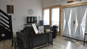 A living room with a sofa, a coffee table, a television, and a door with curtains. - Family/Pet Friendly, Peaceful Cabin, Deck with seasonal Norfork Lake views

 
 (Henderson)