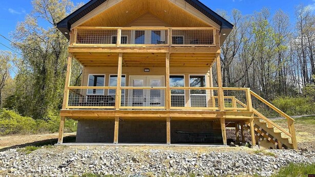 A two-story wooden cabin with a balcony on the upper floor, a covered porch, and a staircase leading to the entrance. - Family/Pet Friendly, Peaceful Cabin, Deck with seasonal Norfork Lake views

 
 (Henderson)