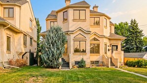 A multi-story house with a prominent front entrance, a staircase leading to the main door, and a well-maintained lawn.