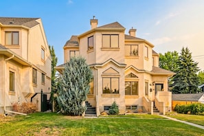 A multi-story house with a prominent front entrance, a staircase leading to the main door, and a well-maintained lawn.