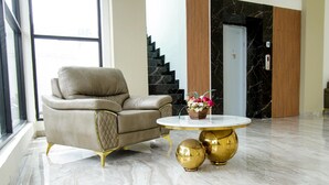 A modern lobby with a leather armchair, a marble floor, and a round gold table with a vase of flowers. - Hotel Sepanak by Amazing (Central Curup)