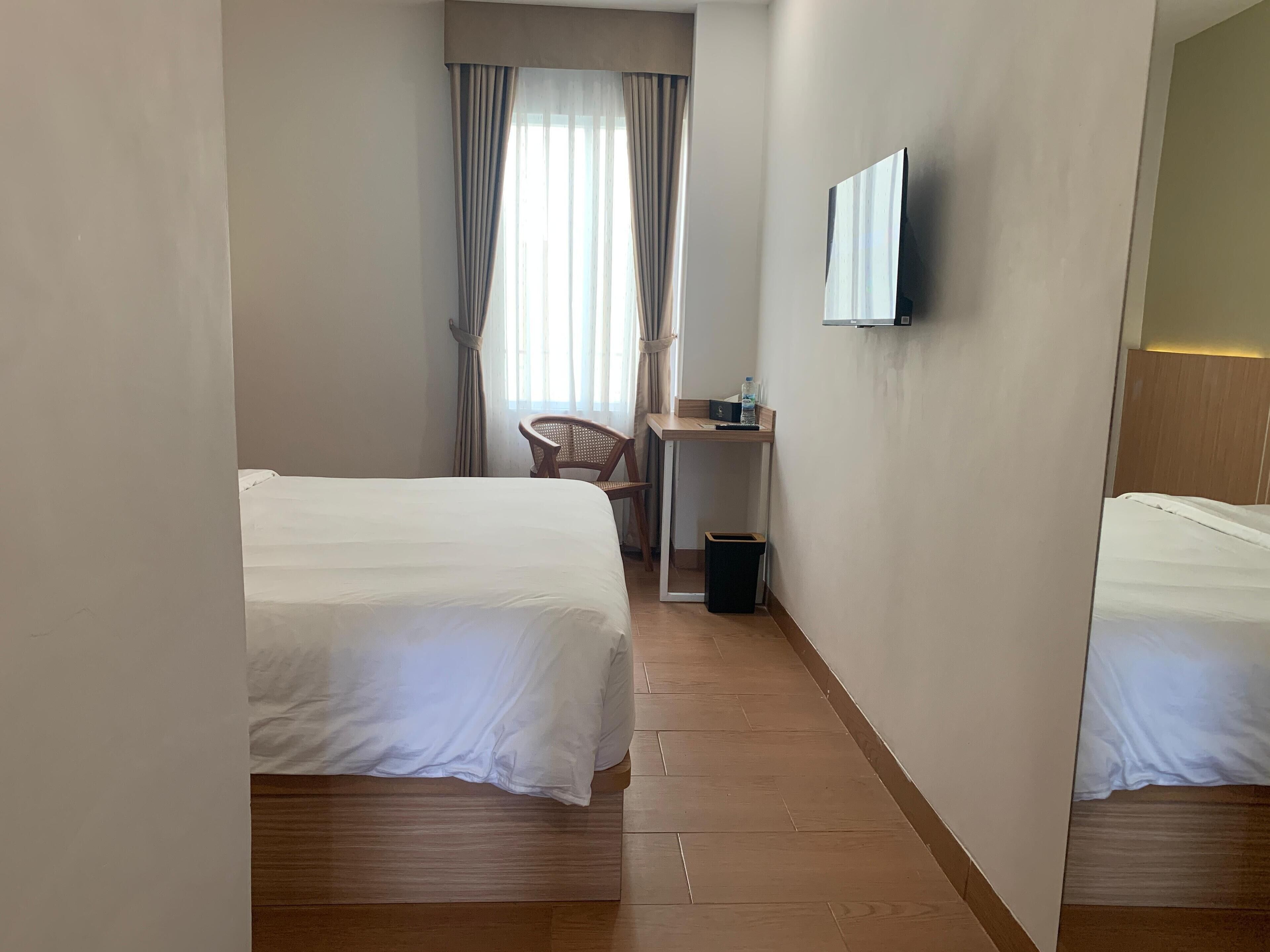 A hotel room with two beds, a desk, a chair, and a TV mounted on the wall.