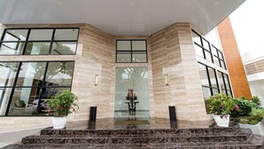 A modern building entrance with a glass door, marble steps, and potted plants. - Hotel Sepanak by Amazing (Central Curup)