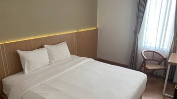 Una cama bien hecha con sábanas blancas, un cabecero de madera y una mesita de noche con una silla.