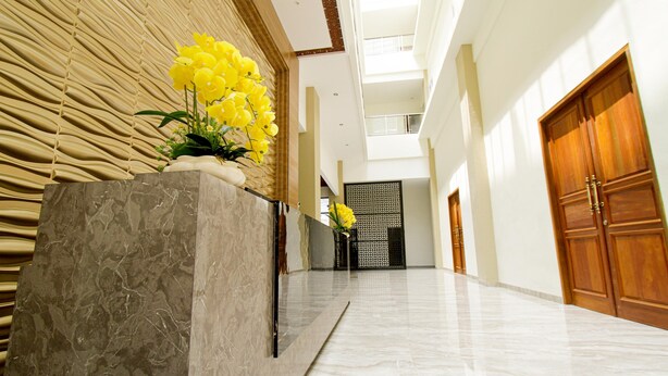 A spacious, modern lobby with a marble floor, a reception desk with a vase of yellow flowers, and a traditional wooden door. - Hotel Sepanak by Amazing (Central Curup)