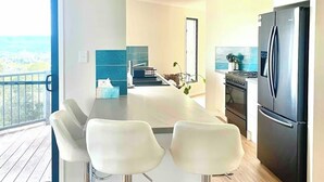 A modern kitchen with a black refrigerator, a dining area with white chairs, and a view of the ocean through a large window.