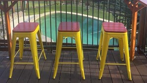 A wooden deck with three yellow stools and a pool in the background.