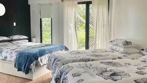 A bedroom with two beds, a ceiling fan, and a large window with curtains.
