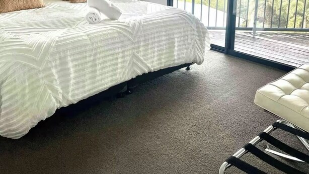 A modern hotel room with a large bed, a white chair, and a balcony with a view.