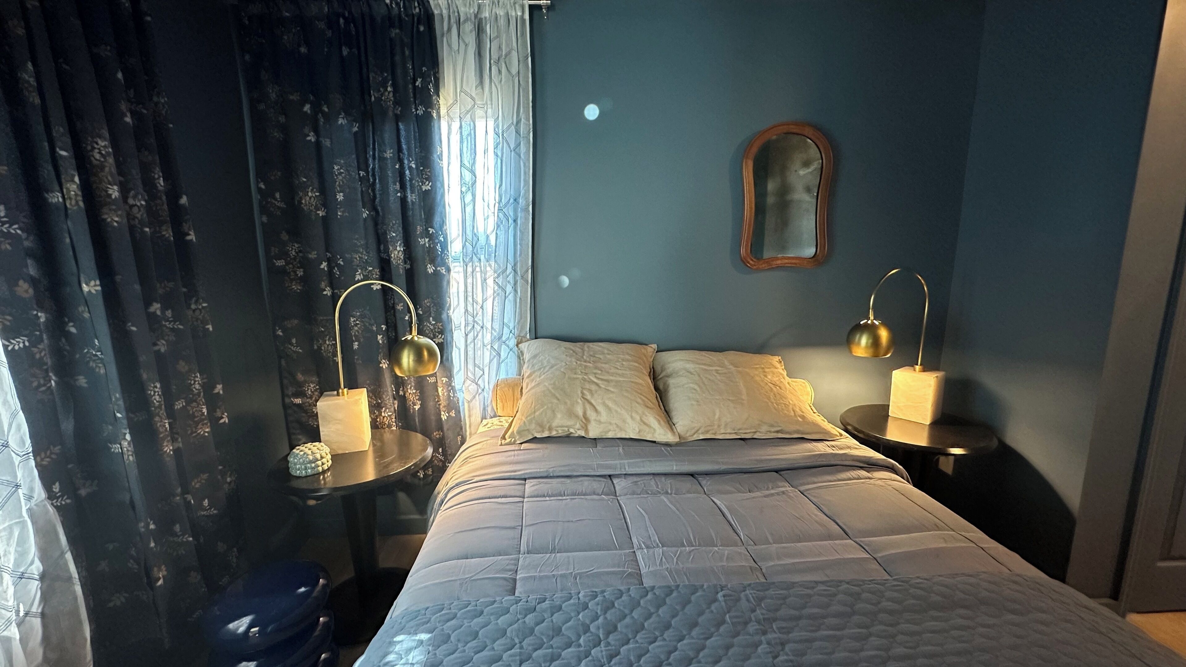 A bedroom with a bed, two bedside tables, a mirror, and a window with curtains.