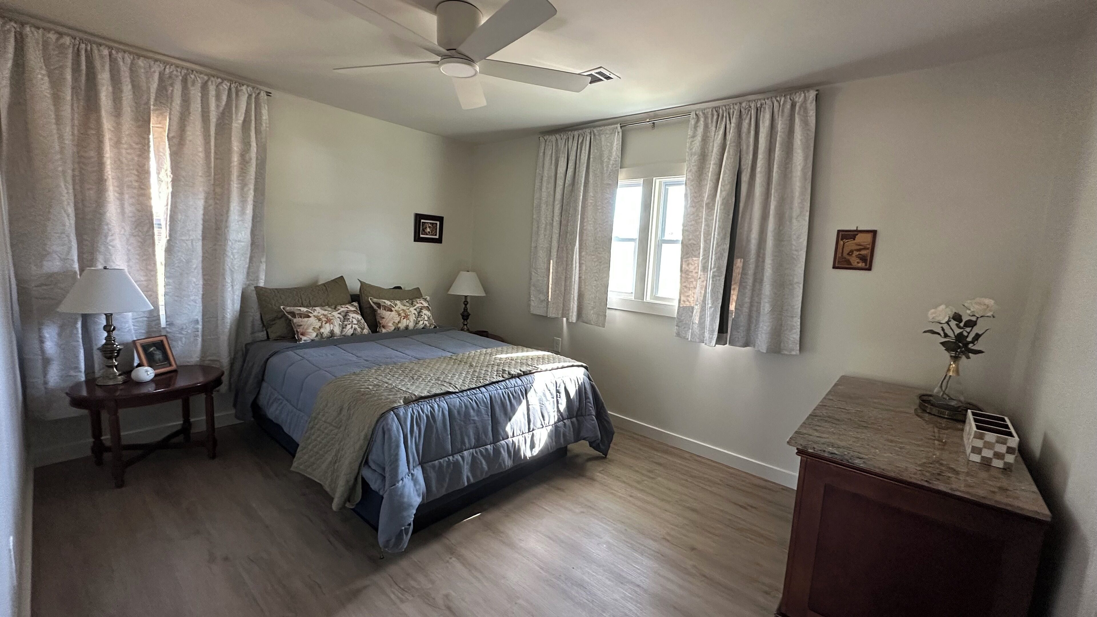 A bedroom with a bed, two bedside tables, a ceiling fan, and a nightstand with a lamp.
