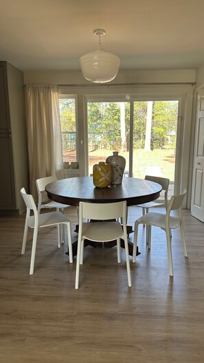 A round dining table with white chairs, a white ceiling light, and a view of a garden through large windows. - Downtown Perry Cozy 4/3 house with fenced backyard (Perry)