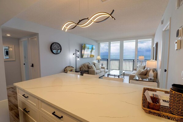 A spacious living area with a large island, a balcony with a view, and a modern light fixture.