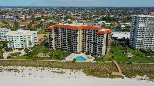 A high-rise hotel with multiple balconies, a swimming pool, and a beach view.