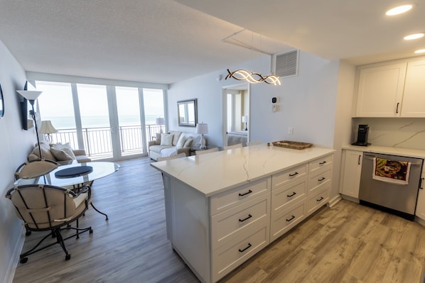 A modern kitchen with a large island, white cabinetry, and a view to the outside.